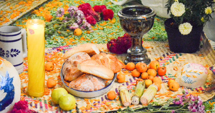 Part of a table with a candle, bread, two melons, many mandarine, a bowl, flowers and others foods (which aren't clear for people who know little about Day of the Dead).
